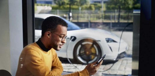 Porsche launches Porsche Finder, its pre-owned vehicle search platform - Pictured here is an African American man operating his smartphone, with his Taycan charging in b.g. Credit: PCNA