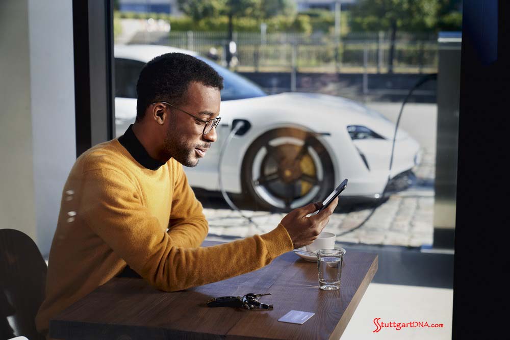 Porsche launches Porsche Finder, its pre-owned vehicle search platform - Pictured here is an African American man operating his smartphone, with his Taycan charging in b.g. Credit: PCNA