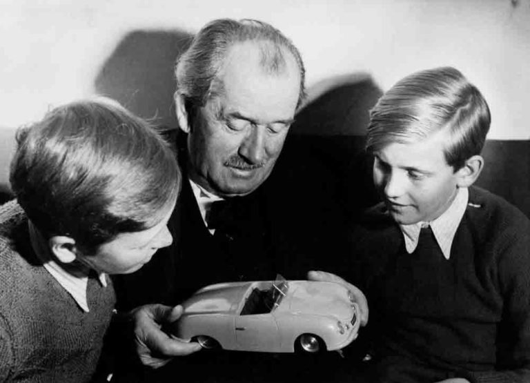 Ferdinand Porsche Biography: Seen here in this intimate family portrait are Prof. Ferdinand Porsche with grandchildren Ferdinand Alexander ("Butzi") Porsche (left) and Ferdinand Piëch (right), ca. 1949. Prof. Porsche holds in his hands the symbolic genesis of the family's automobile manufacturing company, a model of immortal Porsche No 1. Credit: Porsche AG Archives