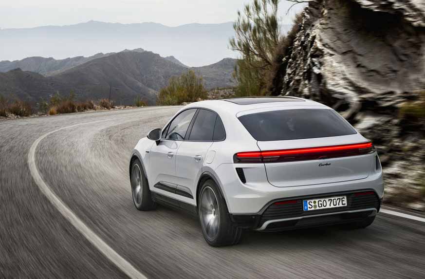 Depicted here is a white Macan EV Turbo, left-rear corner, tooling along a twisty mountain road. Credit: Porsche AG